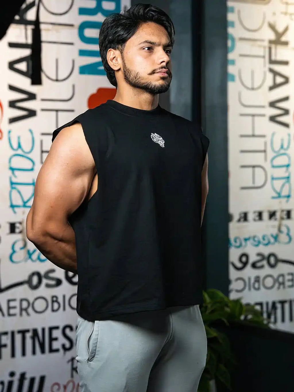 Athletic man in black sleeveless gym shirt and light joggers standing in fitness studio